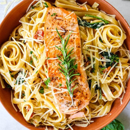 Creamy salmon pasta in tuscan sauce with tomatoes, spinach, and basil.